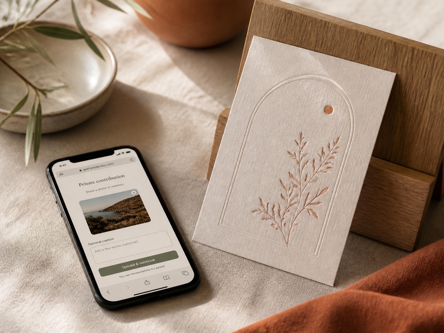 A contributor uploading a photo through the private website, beside a finished cream card resting on an oak display stand